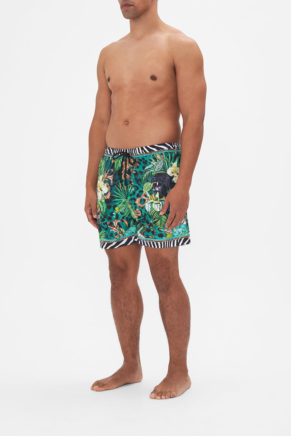 Side view of model wearing Hotel Franks by CAMILLA mens green boardshorts in Sing my Song print