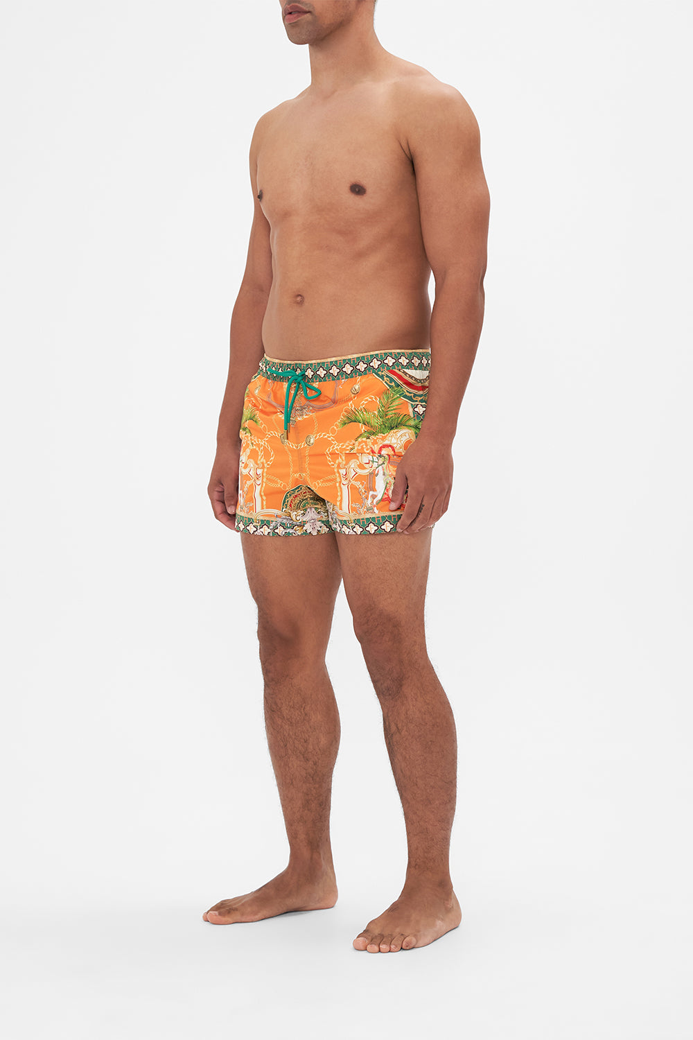 Side view of model wearing Hotel Franks by CAMILLA silk mens short boardshorts in orange Dancing With The Bulls print