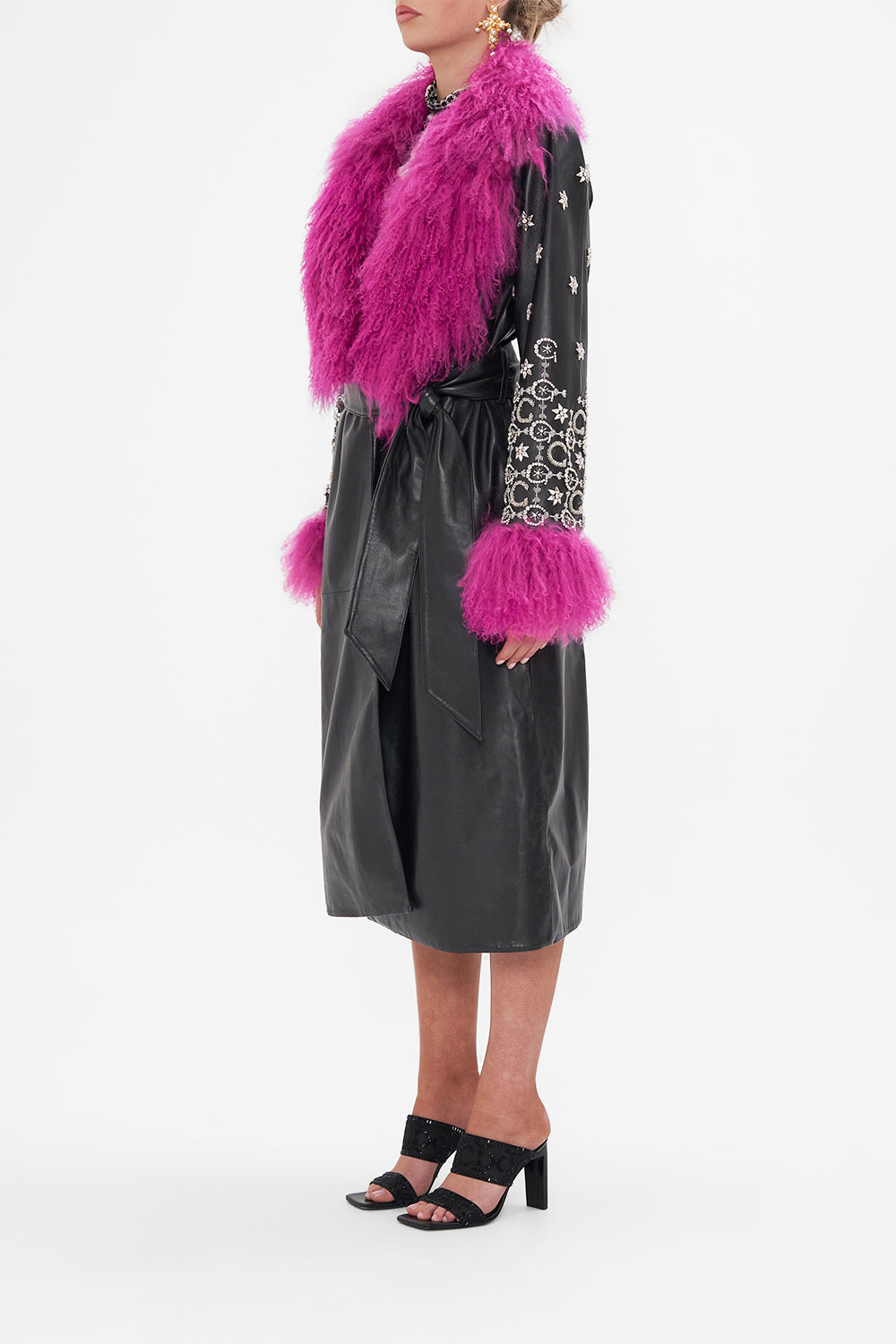 Side view of model wearing CAMILLA black leather trench with fur cuffs and collar