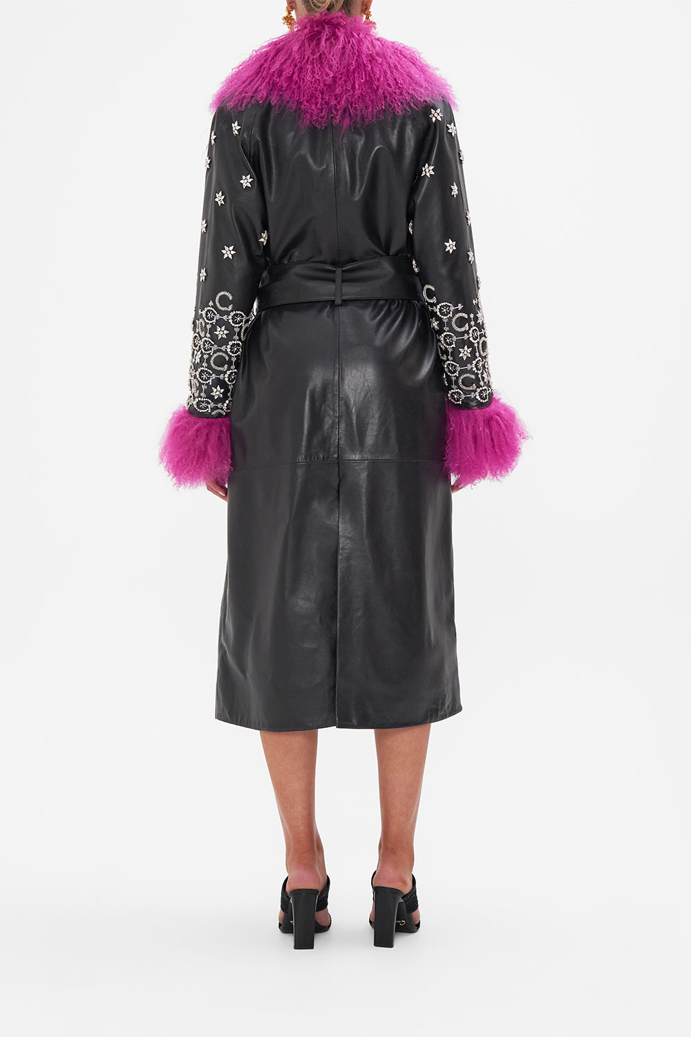Back view of model wearing CAMILLA black leather trench with fur cuffs and collar