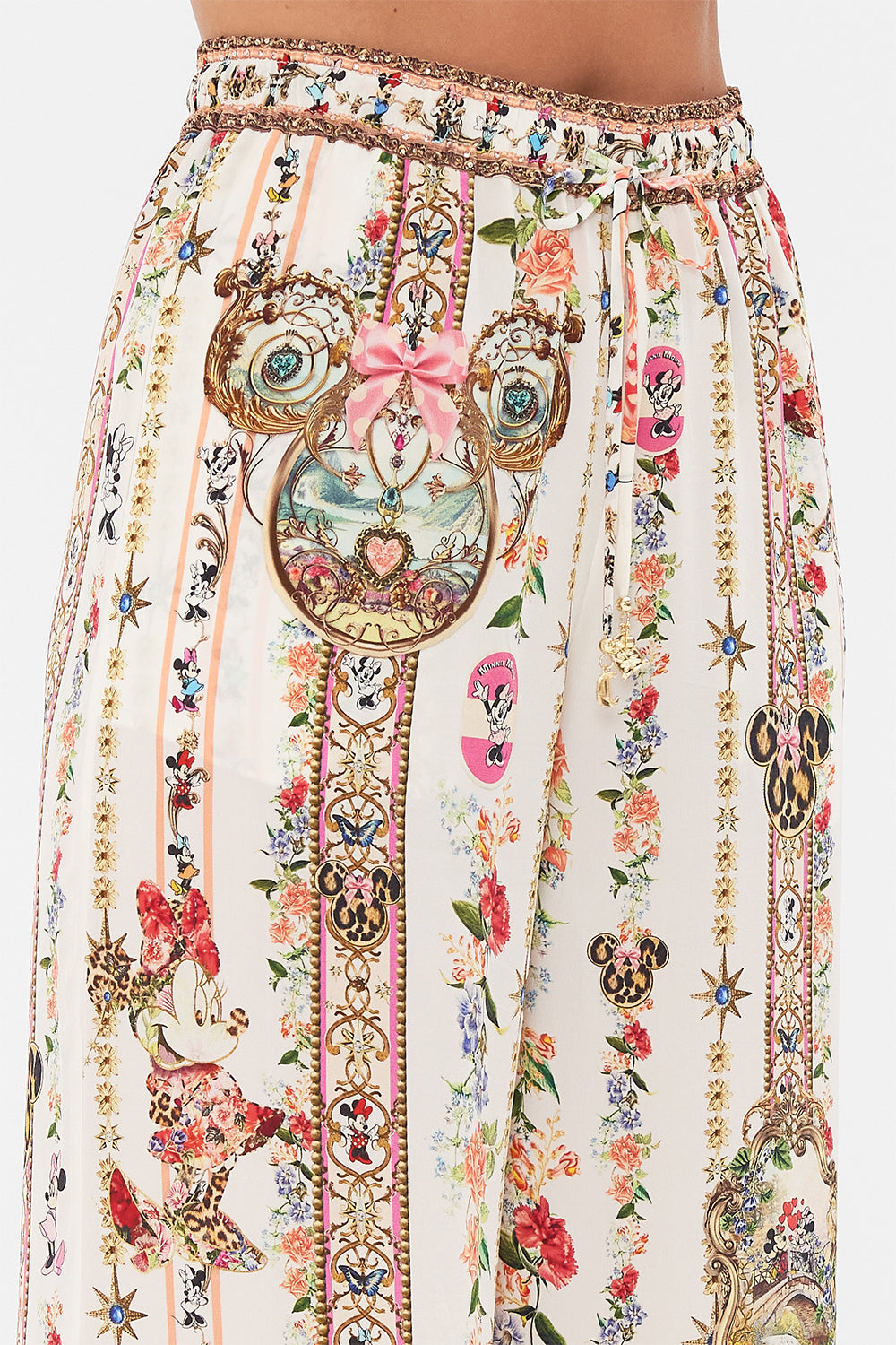Detail view of model wearing Disney x CAMILLA silk pants in Minnie Magic Forever print